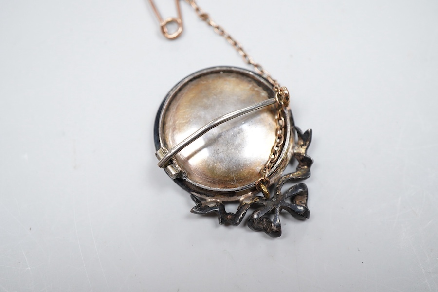 A painted miniature and seed pearl brooch, late 19th century, set with a glazed circular portrait miniature on ivory depicting a lady dressed in the 18th century manner, within a mount topped with a ribbon bow, set with